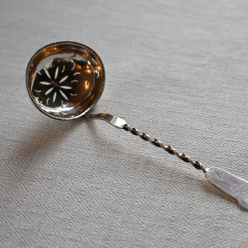 An old silver sugar spoon on a linen cloth
